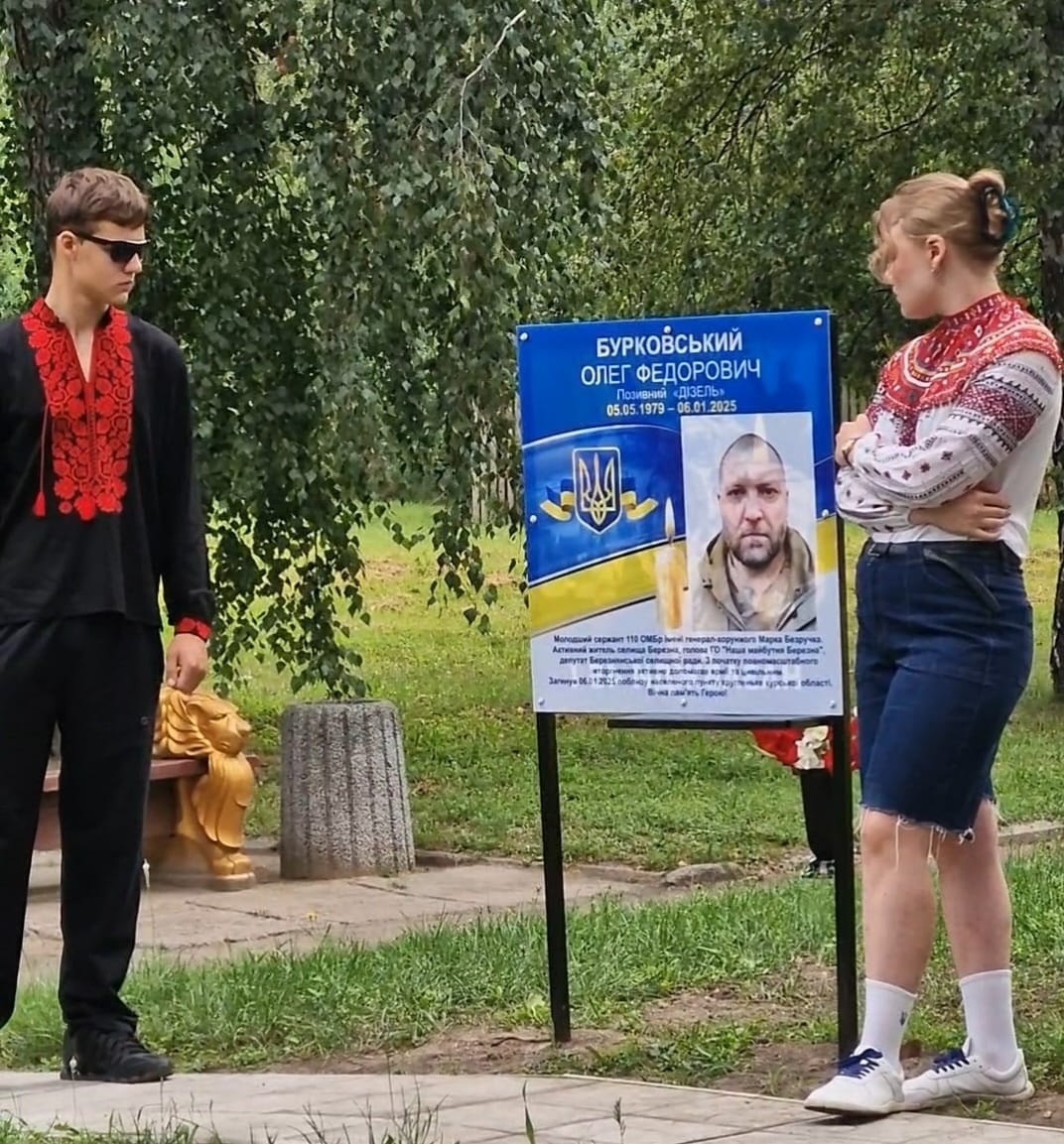 Олексій та Каріна Бурковські біля банера із зображенням батька на Алеї Героїв у Березні